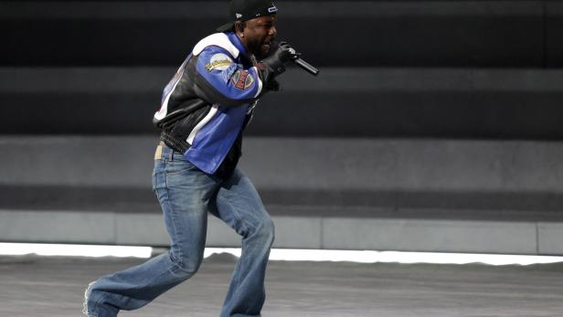 Der Rapper auf der Bühne mit bunter Lederjacke, Turnschuhen und weit ausgestellter Schlaghose.