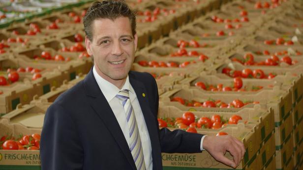 Ein Mann im Anzug steht vor Kisten mit frischen Tomaten aus Österreich.