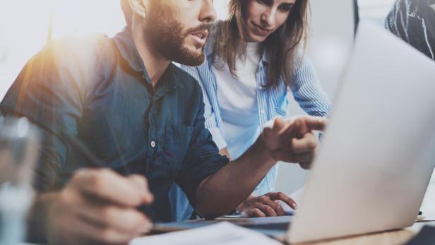 Group of coworkers sitting at the wooden table and working together on new startup project in modern loft office.Horizontal.Blurred background.Cropped.