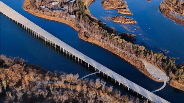 Luftaufnahme einer langen, geraden Brücke, die sich durch eine Seenlandschaft schlängelt.