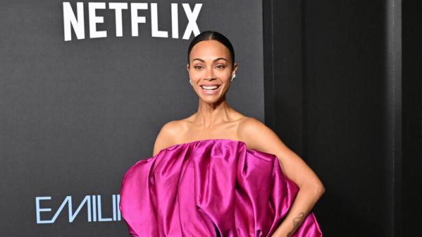 Zoe Saldaña in einem pinkfarbenen Oberteil und einem schwarzen Rock auf dem roten Teppich.