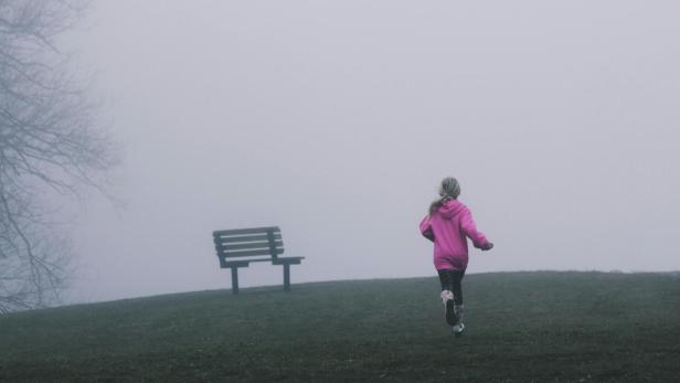 Kleines Mädchen läuft auf einer Wiese im nebel einer Holzbank entgegen. 