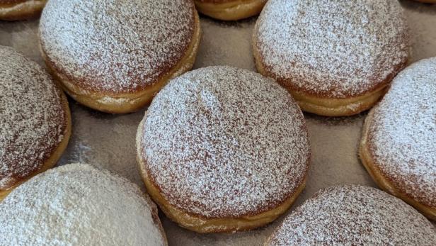 Mehrere Berliner Pfannkuchen, dick mit Puderzucker bestäubt, liegen auf einem Backblech.
