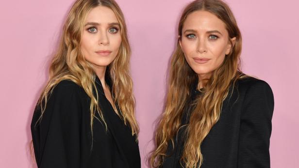 Die Zwillinge Mary-Kate und Ashley Olsen posieren vor einem rosa Hintergrund.