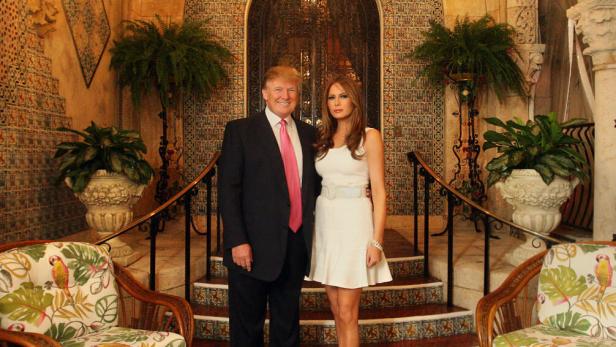 Trump und seine Frau sehen auf einem Teppich vor einer mit Fliesen gekachelten Stufe. Der Türbogen im Hintergrund und die Mauer wirken spanisch-maurisch
