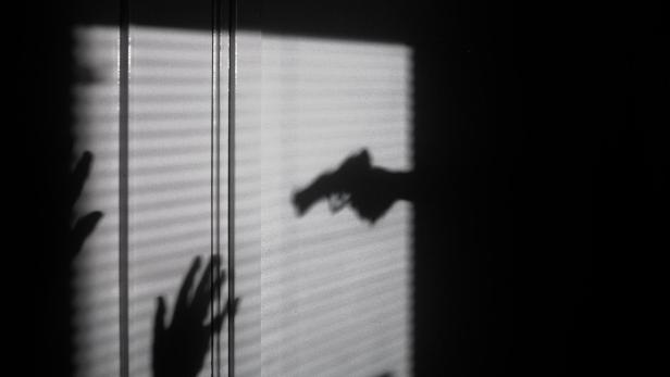 Ein Schatten von einer Pistole und einer Angegriffenen.