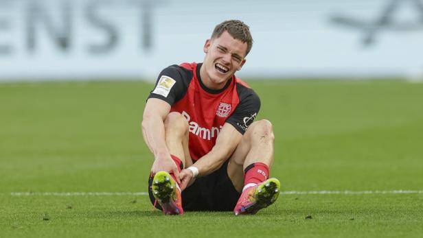 Ein Fußballspieler sitzt auf dem Rasen und scheint Schmerzen zu haben.
