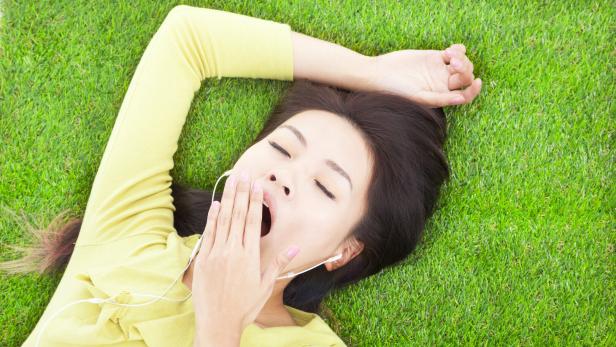 Eine Frau liegt im Gras und gähnt.