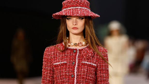 Ein Model mit rotem Tweed-Hut und passendem Blazer auf dem Laufsteg.