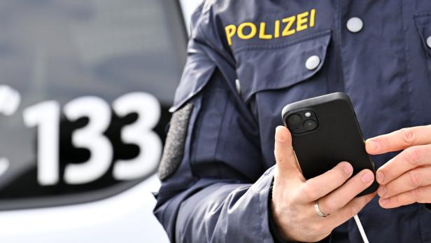 Polizist vor Polizeiauto mit Notruf im Hintergrund
