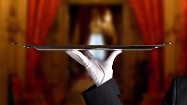 Ein Kellner hält ein leeres, silbernes Tablett.