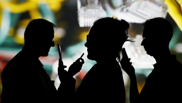 FILE PHOTO: People look at data on their mobiles as internet wire cables on switch hub are shown in background Menschen sehen sich Daten auf ihren Handys an.