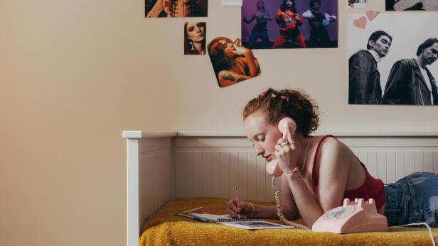 Millennials und Gen Z: Jeder Sechste zieht zu den Eltern zurück Junge Frau liegt mit einem Telefon am Ohr im Bett im Jugendzimmer