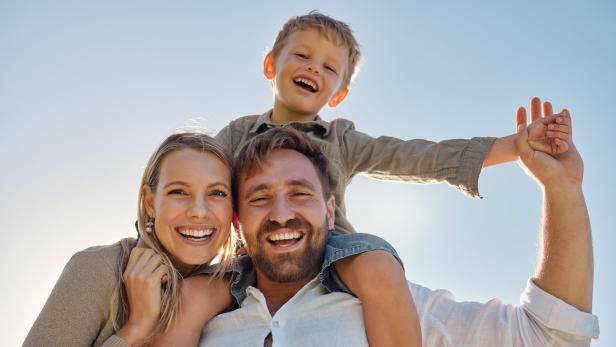 Family, mother and father with child, for holiday, vacation and being happy together outdoor. Portrait, mama and dad with kid for quality time, travel and bonding being loving, carry boy and have fun Vater, Mutter und ein Kind lachen in die Kamera.