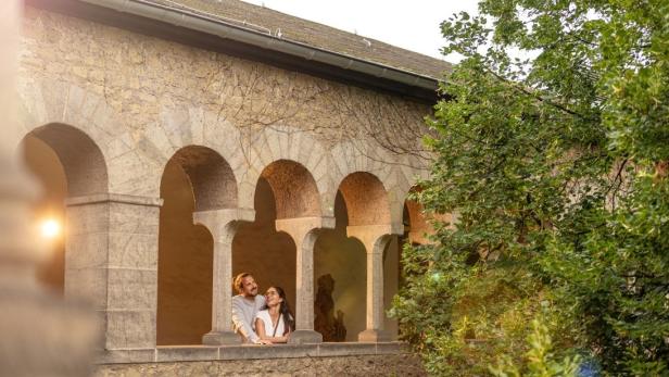 Ein heterosexuelles Paar umarmt sich in einem offenen Gang und schaut aus der Wandöffnung draußen.