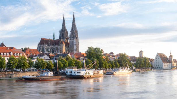 Blick auf die Stadt Regensburg, Deutschland, mit Schiffen, die auf der Donau fahren, umgeben von historischen Gebäuden.