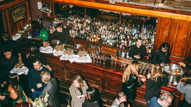 Blick von oben auf eine belebte Bar mit vielen Gästen und einer großen Auswahl an Spirituosen.