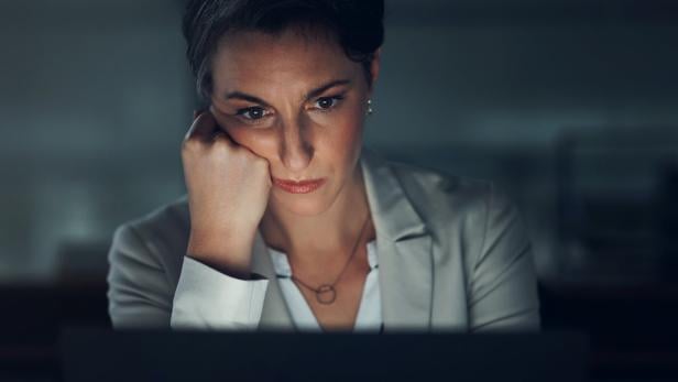 Eine müde Frau schaut im Dunkeln auf einen Computer. 
