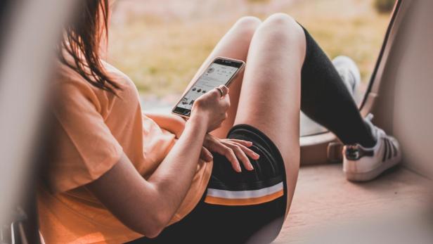 Studie zeigt: WhatsApp und soziale Medien belasten Freundschaft Junge Frau sitzt mit Handy vor einem Fenster