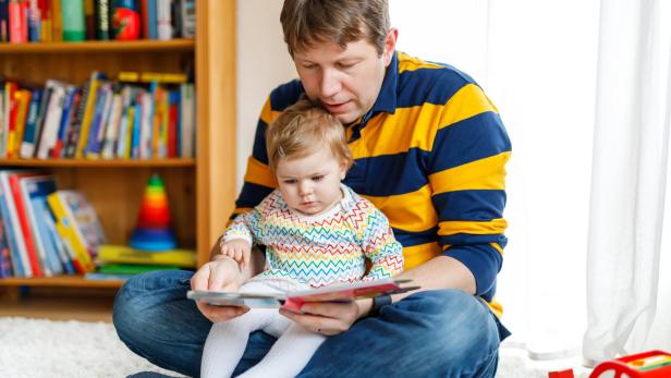 Junger Vater, der mit seiner kleinen Tochter ein Buch liest.