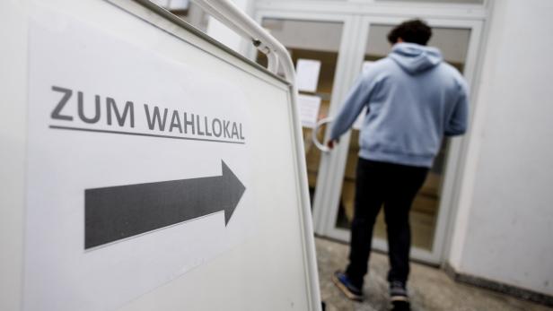 Ein Schild mit der Aufschrift "Zum Wahllokal" und einem Pfeil zeigt die Richtung, während eine Person eintritt.
