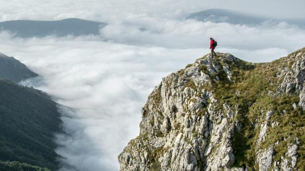 Handy runtergefallen: 20-Jährige hing an Felsen fest Frau in Wanderkleidung steht auf einem Felsen und blickt über die Wolken