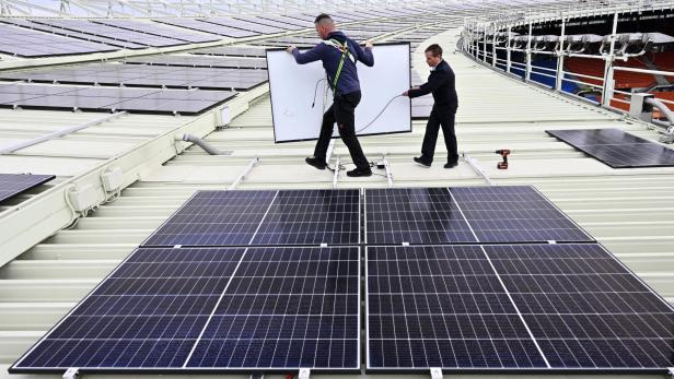Zwei Männer installieren Solarpaneele auf dem Dach eines Stadions.