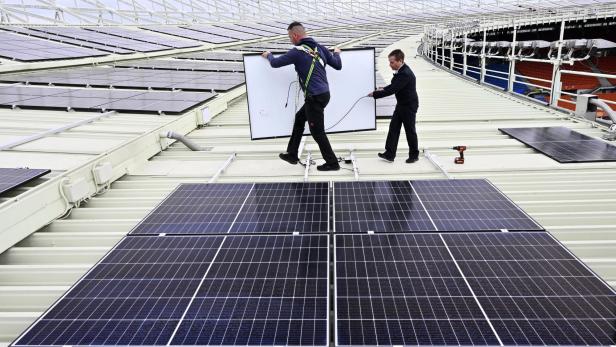 Zwei Männer installieren Solarpaneele auf dem Dach eines Stadions.