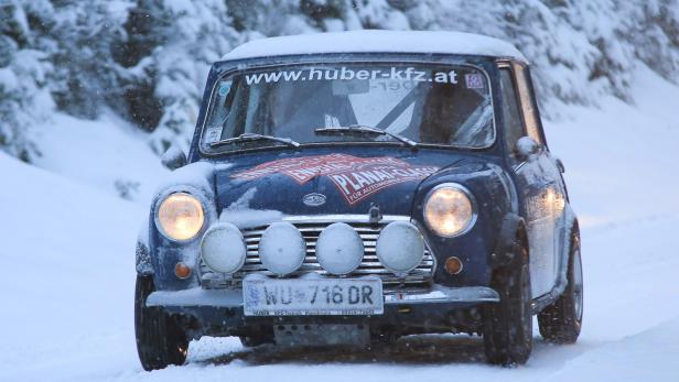 Ein blauer Mini Cooper mit eingeschalteten Scheinwerfern im Schnee.