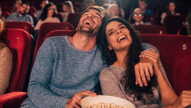 Ein lachendes Paar sitzt mit Popcorn im Kino.