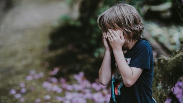 Wegen Bussi: Bub (2) wurde blind auf einem Auge – durch Herpes Kleiner blonder Junge steht im Grünen und hält sich die Augen zu