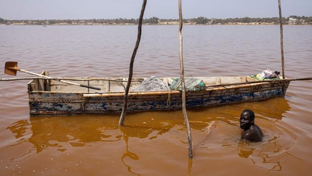 TOPSHOT-SENEGAL-ENVIRONMENT-ECONOMY-TOURISM Ein Mann steht im rosafarbenen Wasser und hält ein Boot mit Salzladung fest.