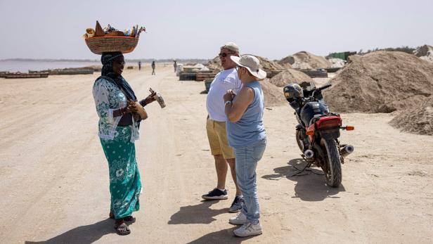 SENEGAL-ENVIRONMENT-ECONOMY-TOURISM Eine Frau verkauft Souvenirs an Touristen in der Nähe eines Motorrads und Sandhügeln.