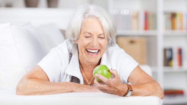 Gesund mit 70: Was fitte Senioren essen – und was nicht Ältere lachende Frau mit grünem Apfel in der Hand