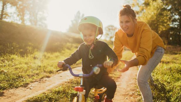 Mama hilft Kind beim Radfahren. 
