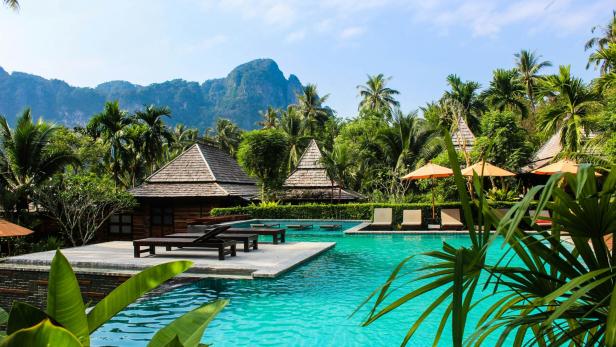 Kleine Hütten und Sonnenliegen inmitten eines türkisen Pools, der umringt ist von Palmen
