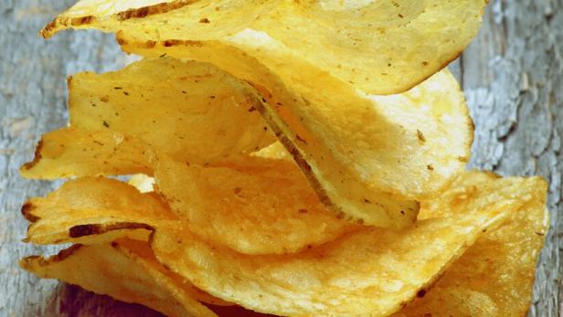 Ein Stapel goldgelber Kartoffelchips auf einem Holztisch.