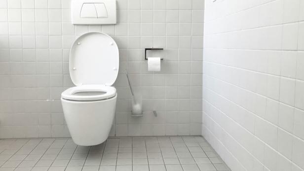 Die junge Frau lebt freiwillig nach Feierabend auf sechs Quadratmetern in einem Kunden-WC eines Möbelladens. Weiß gefliestes WC mit Toilettenpapierhalter, Klobürste