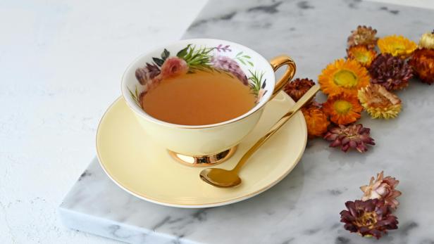 Aufgrund eines "beruflichen Konflikts" wollte eine Frau ihre Arbeitskollegin aus dem Weg räumen – mit vergiftetem Tee. Teetasse mit Blumenprint auf einer Mamorplatte, daneben liegen getrocknete Blumen