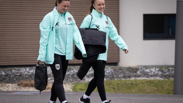 Zwei junge Frauen in Trainingskleidung gehen lächelnd nebeneinander her.