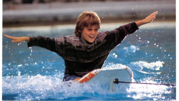 Ein lächelnder Junge reitet auf einem Surfbrett im Wasser, Szene aus dem Film „Free Willy“.