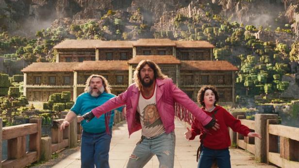 Jason Momoa, Jack Black und ein Kind stehen vor einem Gebäude im Minecraft-Stil.