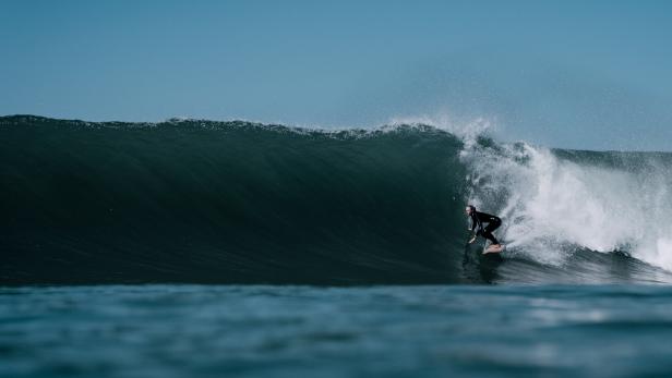 Ein Surfer reitet auf einer großen Welle unter blauem Himmel.