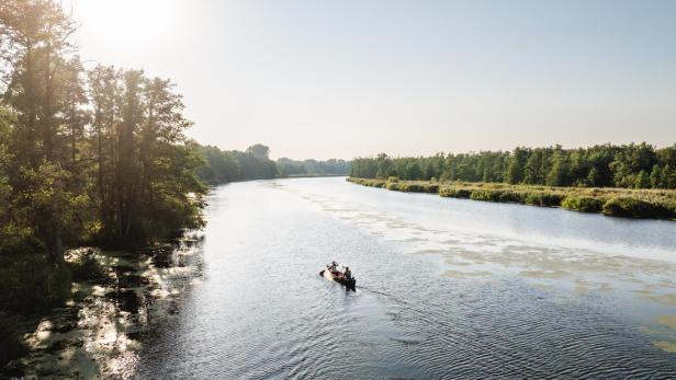 Ein Kanu auf einem breiten Fluss inmitten der Natur im Sonnenuntergang. 
