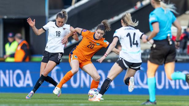 Eine Fußballspielerin im orangefarbenen Trikot kämpft um den Ball.