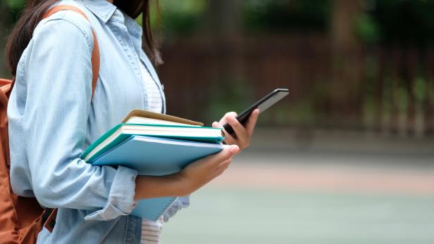 Student girl holding books and smartphone while walking in school campus background, education, back to school concept