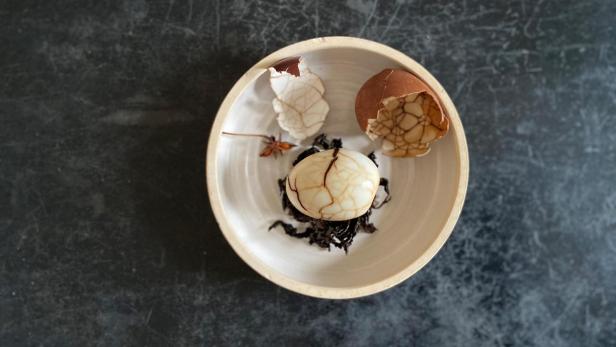 Weißer Teller mit einem marmorierten Tee-Ei, Sternanis und Schwarztee.