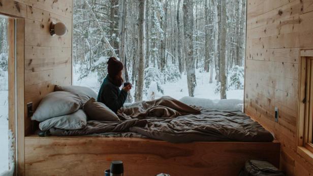 Influencer-Öko-Resort: Frau sitzt in gemütlicher Waldhütte und schaut aus dem Fenster