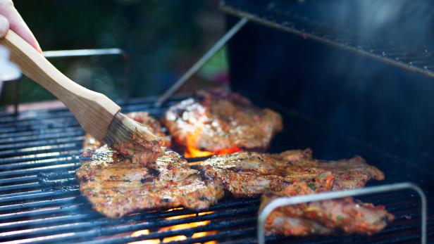 Mit einem Pinsel wird Fleisch auf einem Grill mariniert.