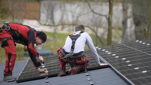 Zwei Arbeiter installieren Solarmodule auf einem Dach.